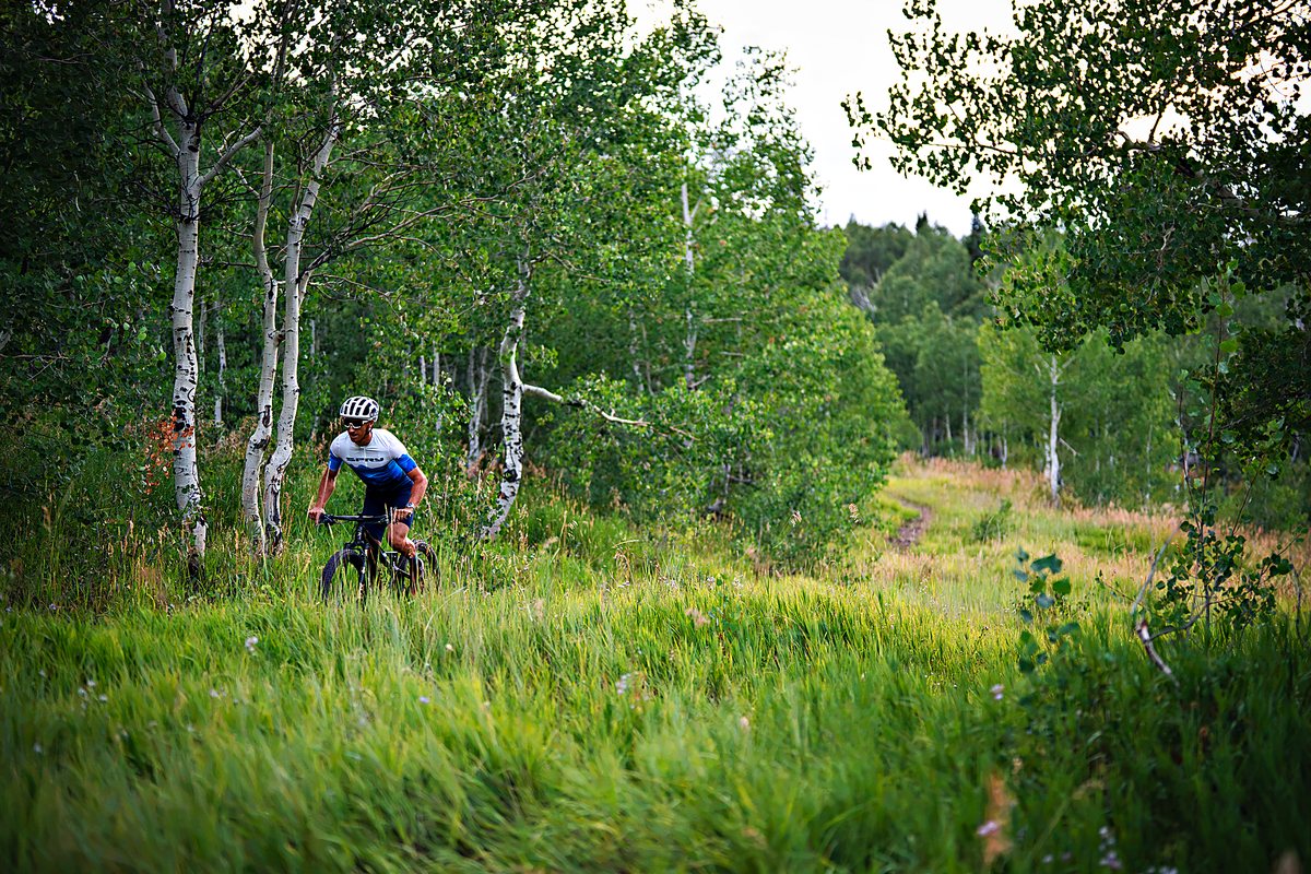 Rider on a Spry mountain bike climbing a grassy singletrack through aspens
