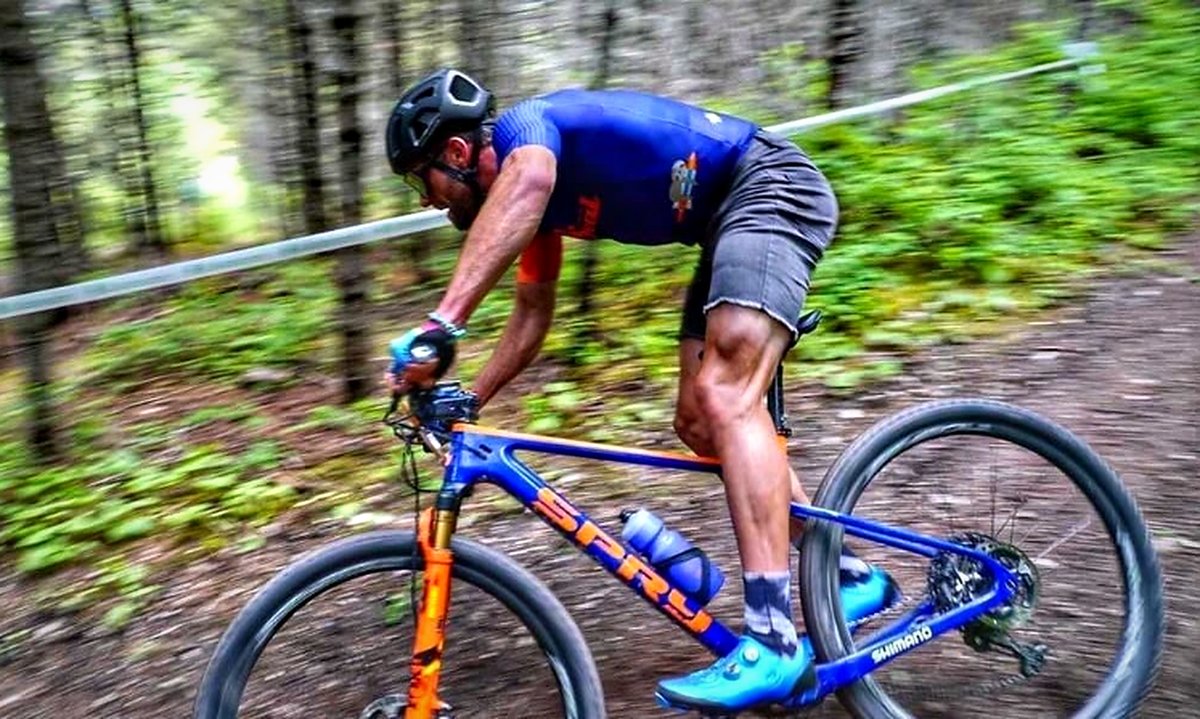 Racer sprinting a blue and orange Spry Hydra hardtail through the trees