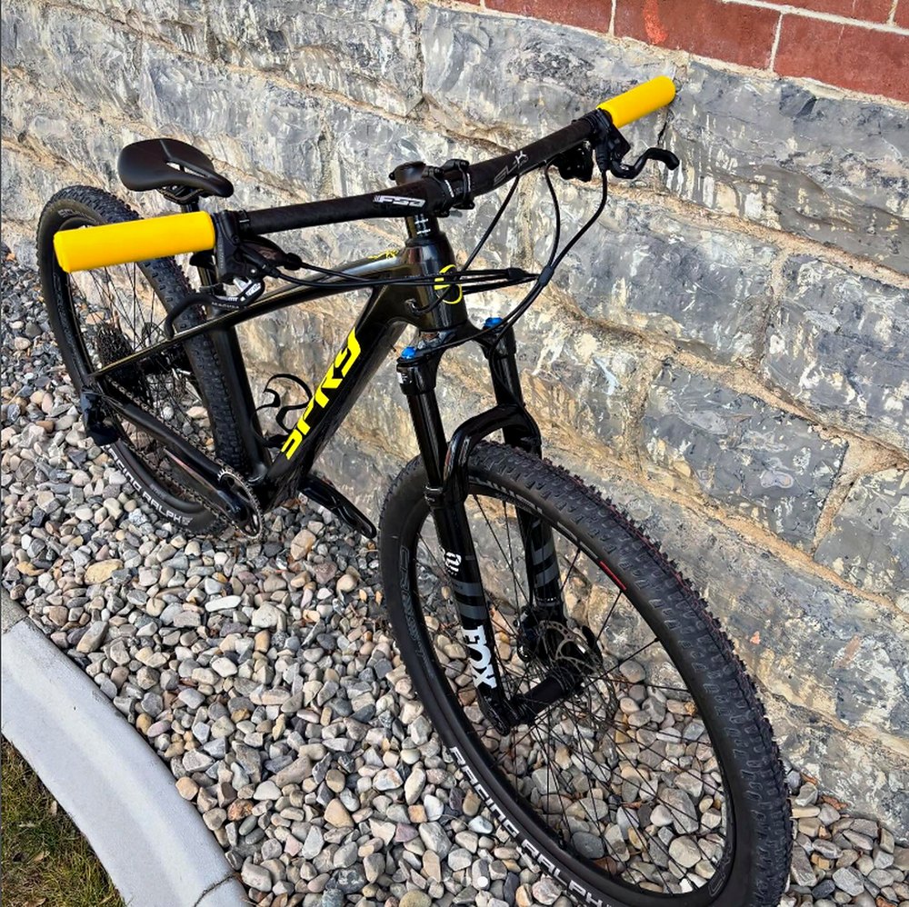Spry Hydra hardtail in black and yellow with a Fox fork, against a stone wall